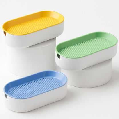 Materas para pasto gatuno en colores amarillo, verde y azul sobre pedestales blancos minimalistas